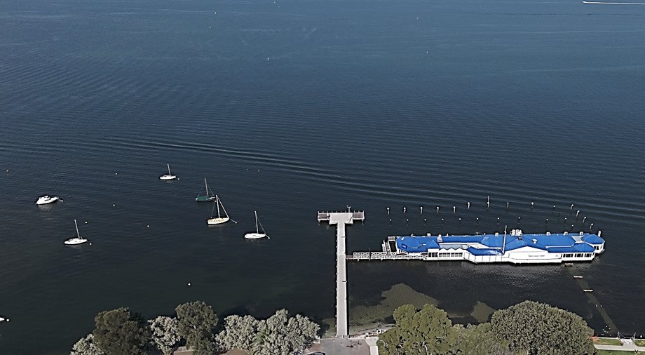 Aerial view of the existing Nedlands Jetty running out into deep water beside the blue-roofed JoJo's building, with yachts moored nearby.